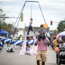 Community member carrying kid on shoulders at Open Streets on Broadway Ave
